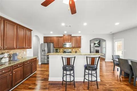 a kitchen with stainless steel appliances granite countertop a kitchen island a stove a dining table and chairs with wooden floor
