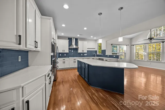 a large kitchen with stainless steel appliances granite countertop a sink dishwasher a stove and white cabinets with wooden floor