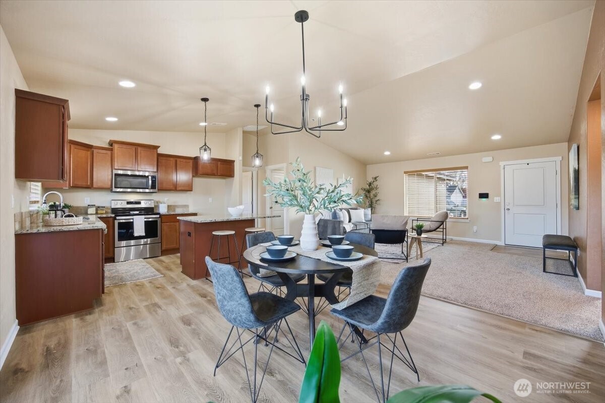 3709 Morehouse Place Pasco, WA 99301 - Photo 11 of 32 a kitchen with stainless steel appliances kitchen island granite countertop a stove a refrigerator a kitchen island a dining table and chairs with wooden floor