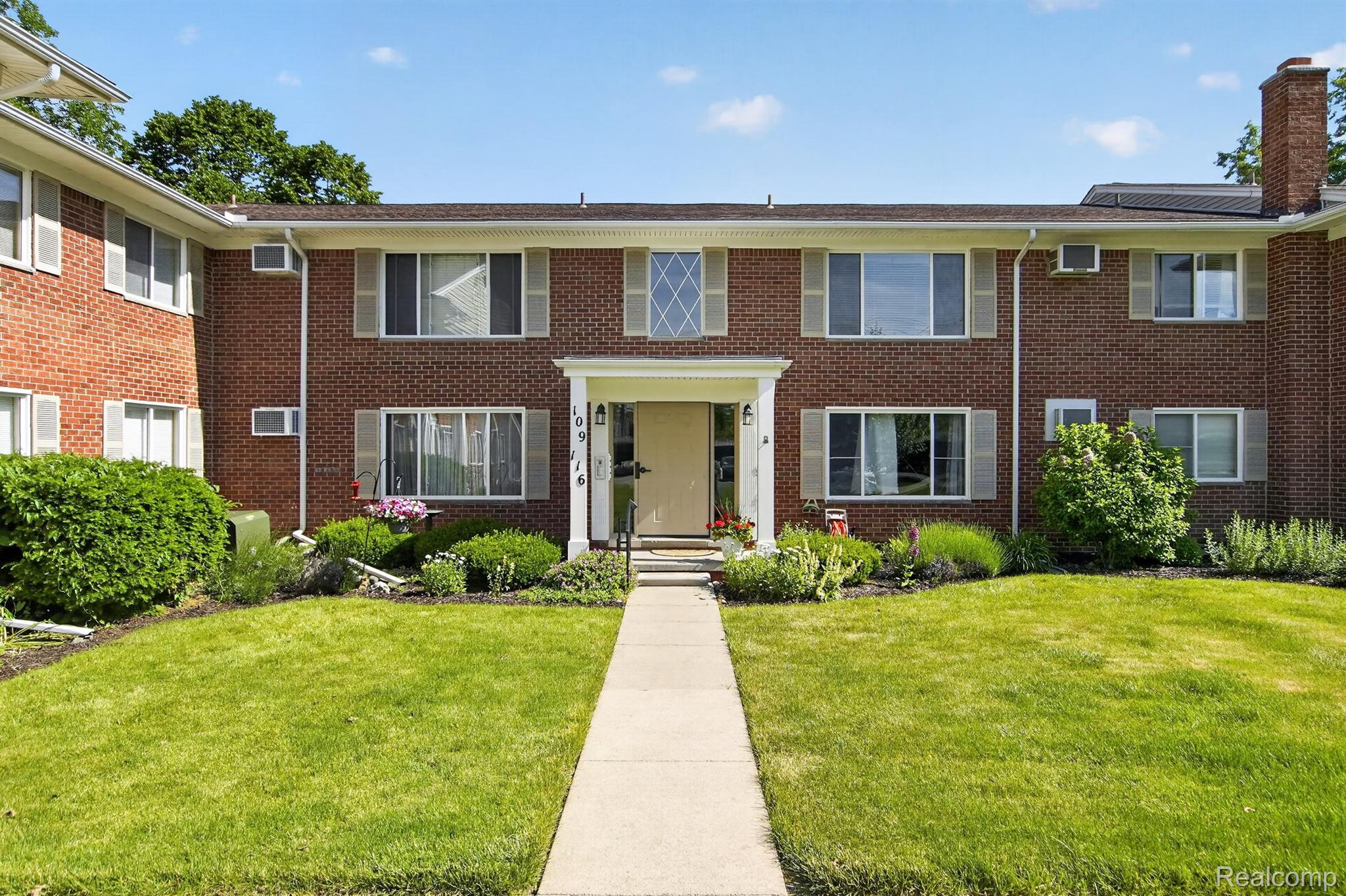 24111 Meridian Road, Unit 116 Grosse Ile, MI 48138 - Photo 3 of 26 Brick facade building featuring a central entrance with white columns, a concrete walkway, and a manicured lawn