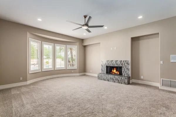 a view of a livingroom with a fireplace a ceiling fan and windows