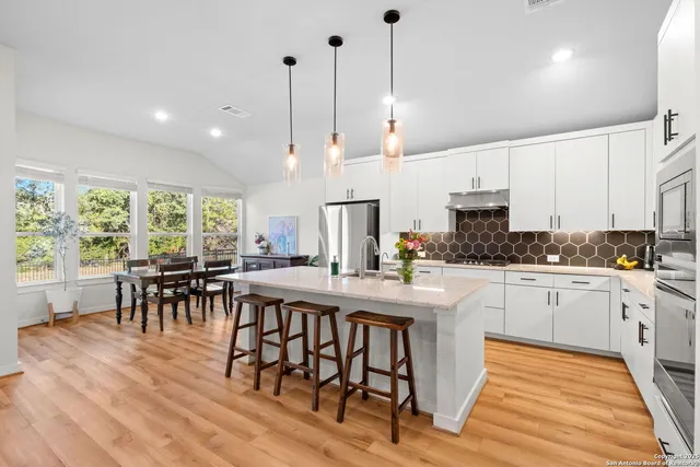 a kitchen with stainless steel appliances granite countertop a stove a refrigerator a kitchen island a dining table and chairs with wooden floor
