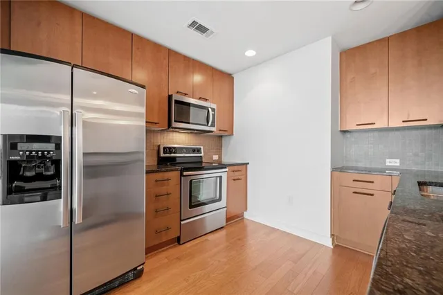 a kitchen with stainless steel appliances granite countertop a refrigerator a stove and a sink with wooden floor