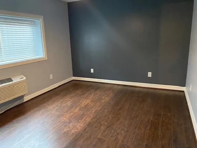 a view of an empty room with wooden floor and a window