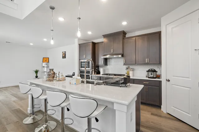 a kitchen with stainless steel appliances granite countertop a sink a stove a refrigerator cabinets and chairs