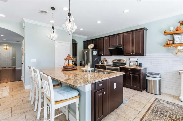 a kitchen with stainless steel appliances granite countertop a stove top oven a sink dishwasher and a refrigerator with wooden cabinets