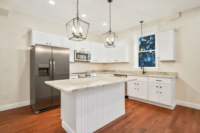 a kitchen with stainless steel appliances granite countertop a sink a stove a refrigerator and island with wooden floor