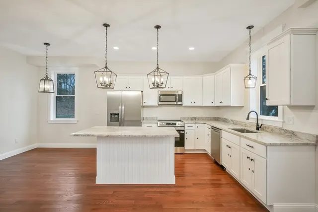 a large kitchen with stainless steel appliances granite countertop a sink a stove and a wooden floor