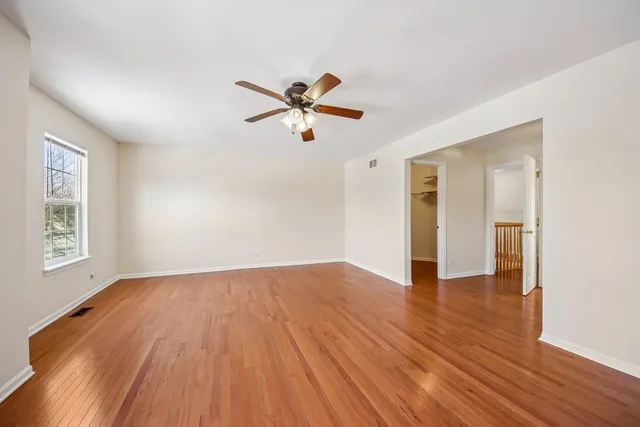 an empty room with wooden floor ceiling fan and windows