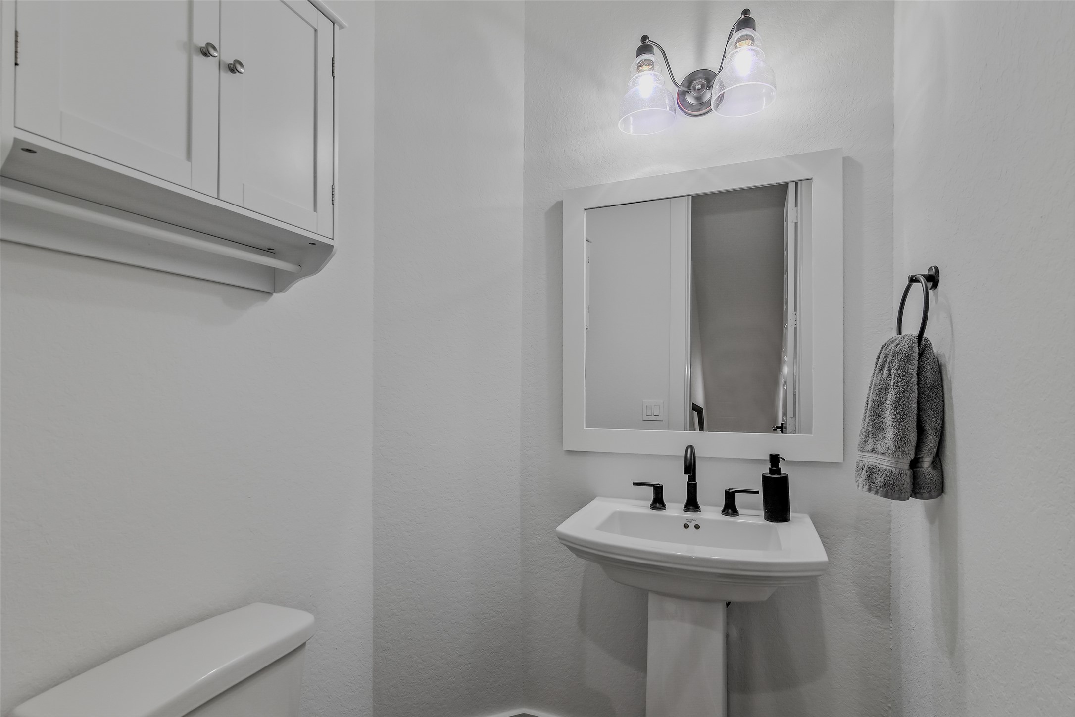 4231 Allen Street Houston, TX 77007 - Photo 9 of 31 The powder room is located in the open concept living space on the second floor. It has convenient overhead cabinets for storage, and a pedestal sink with black matte fixtures for a modern contrast.