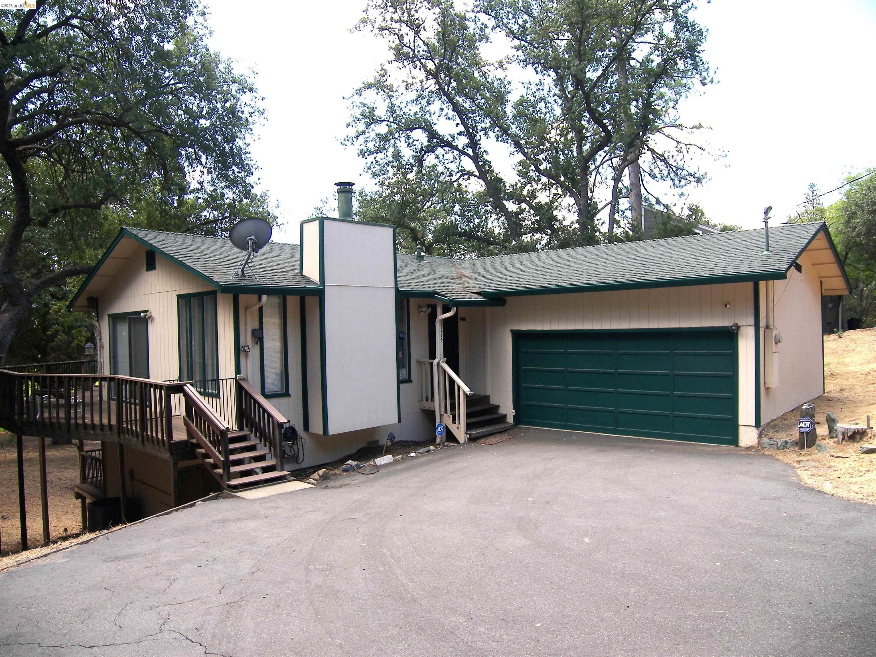 19215 Ferretti Road Groveland, CA 95321 - Photo 38 of 40 Single-story residence featuring a prominent two-car garage with a dark green door, a large wooden deck with railing, and an asphalt driveway