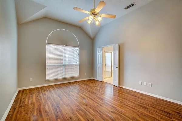 an empty room with wooden floor chandelier fan and windows