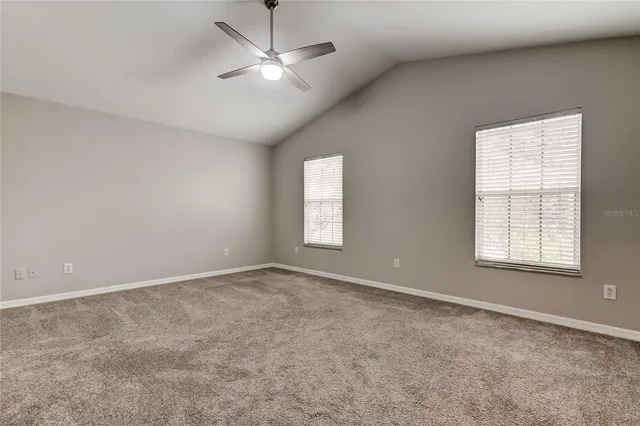an empty room with chandelier fan and windows