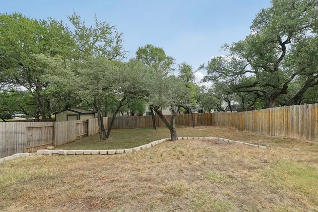 a backyard of a house with large trees and wooden fence