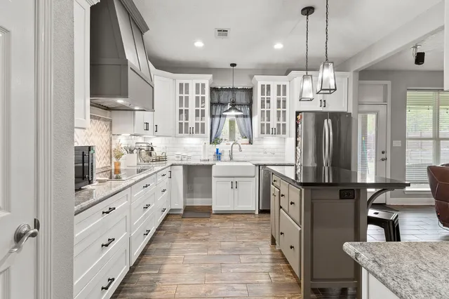 a kitchen with stainless steel appliances kitchen island granite countertop a refrigerator a sink dishwasher a oven with white cabinets and wooden floor