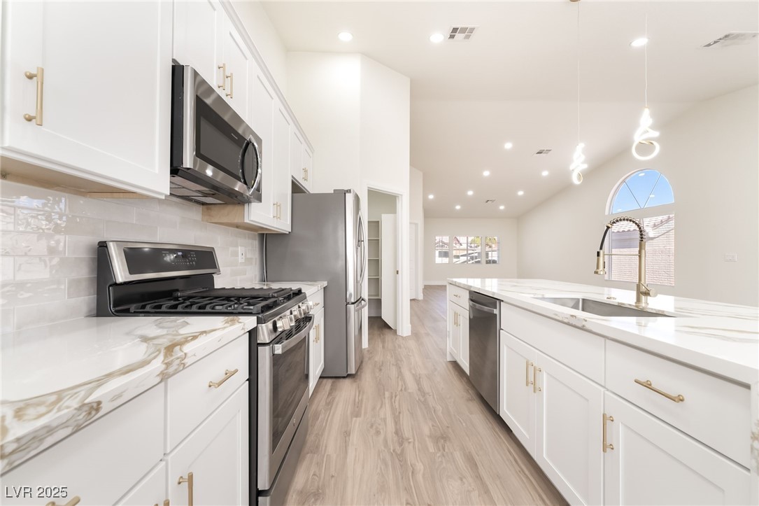 9205 Desert Village Avenue Las Vegas, NV 89147 - Photo 14 of 44 Kitchen featuring appliances with stainless steel finishes, white cabinetry, light stone countertops, decorative light fixtures, and vaulted ceiling