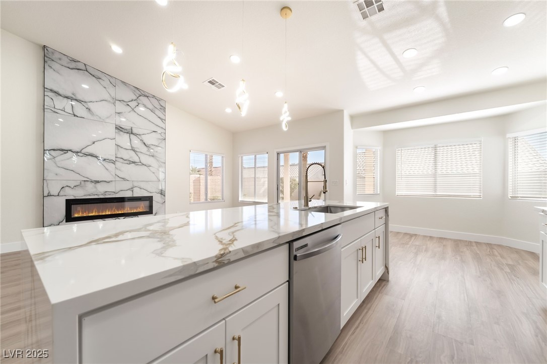 9205 Desert Village Avenue Las Vegas, NV 89147 - Photo 16 of 44 Kitchen featuring light stone counters, decorative light fixtures, stainless steel dishwasher, a fireplace, and white cabinetry