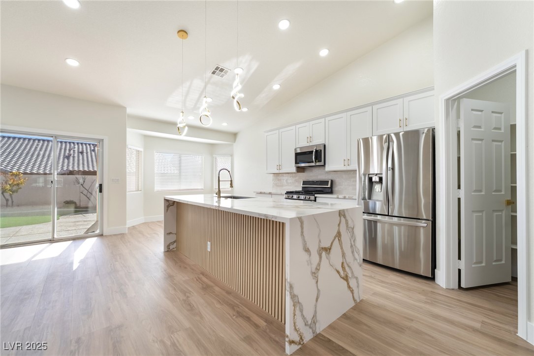 9205 Desert Village Avenue Las Vegas, NV 89147 - Photo 17 of 44 Kitchen featuring stainless steel appliances, recessed lighting, vaulted ceiling, decorative light fixtures, and light stone counters