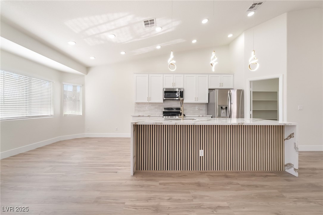 9205 Desert Village Avenue Las Vegas, NV 89147 - Photo 18 of 44 Kitchen featuring white cabinets, a large island, appliances with stainless steel finishes, vaulted ceiling, and light stone countertops