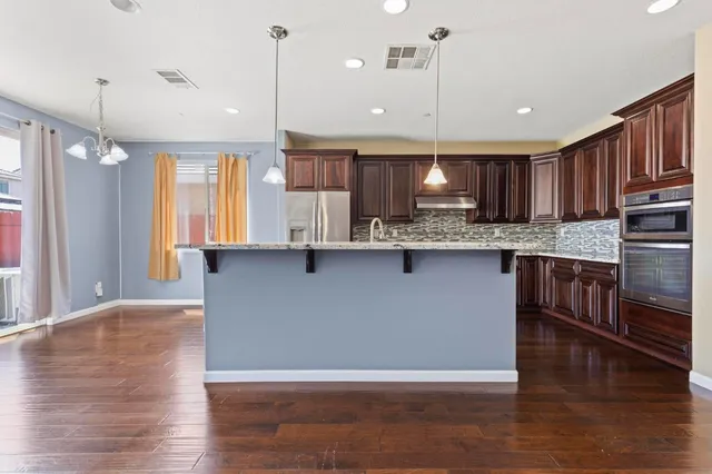 a kitchen with stainless steel appliances granite countertop a sink a stove and a wooden floors