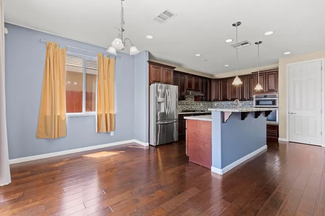 a open kitchen with stainless steel appliances granite countertop a refrigerator a sink dishwasher a oven and a dining table with wooden floor