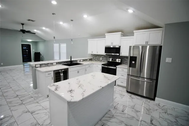 a kitchen that has a sink a microwave a refrigerator and a stove top oven with white cabinets