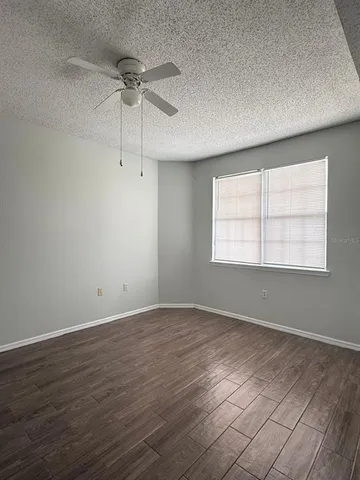 an empty room with wooden floor chandelier fan and windows