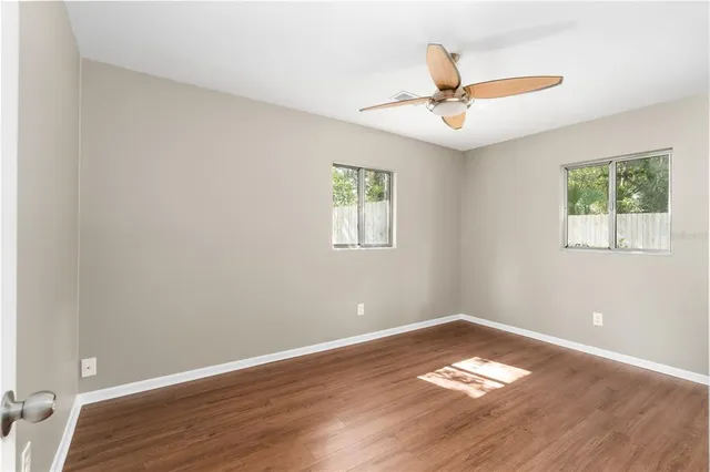 an empty room with wooden floor ceiling fan and window