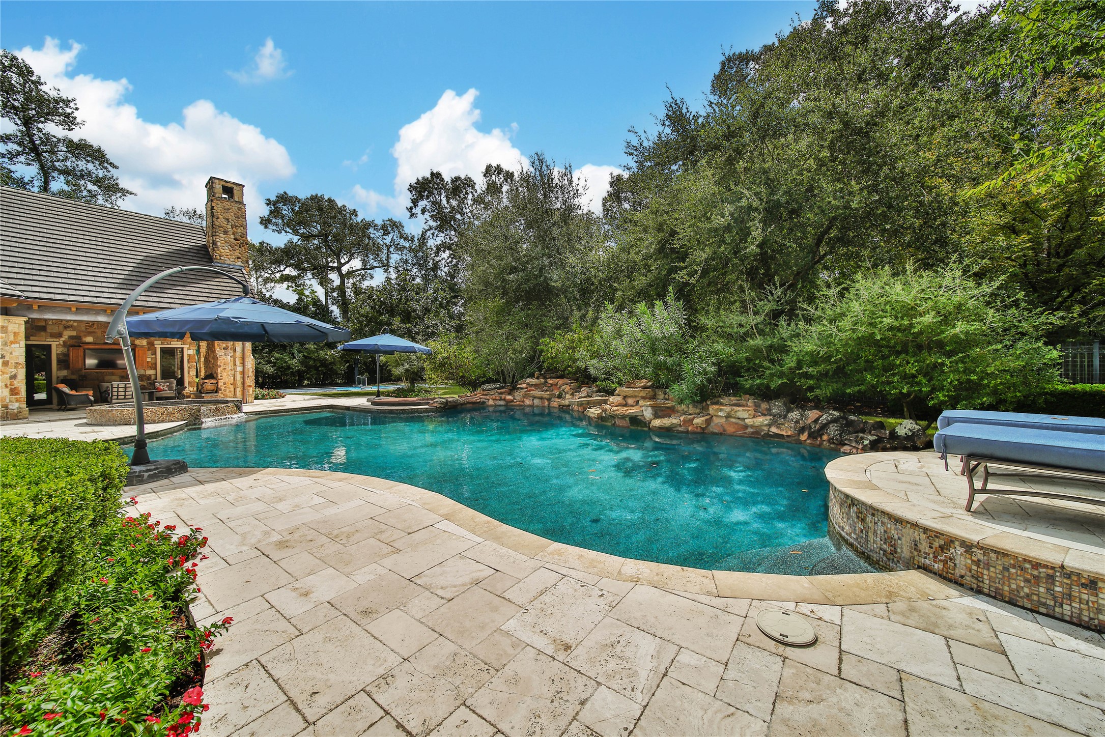 247 South Fazio Way Spring, TX 77389 - Photo 45 of 48 Designed for effortless entertaining, this remarkable backyard retreat features an impressive travertine patio, elevated spa, custom pool, and multiple lounge areas, all within a serene wooded setting that creates a true outdoor sanctuary.