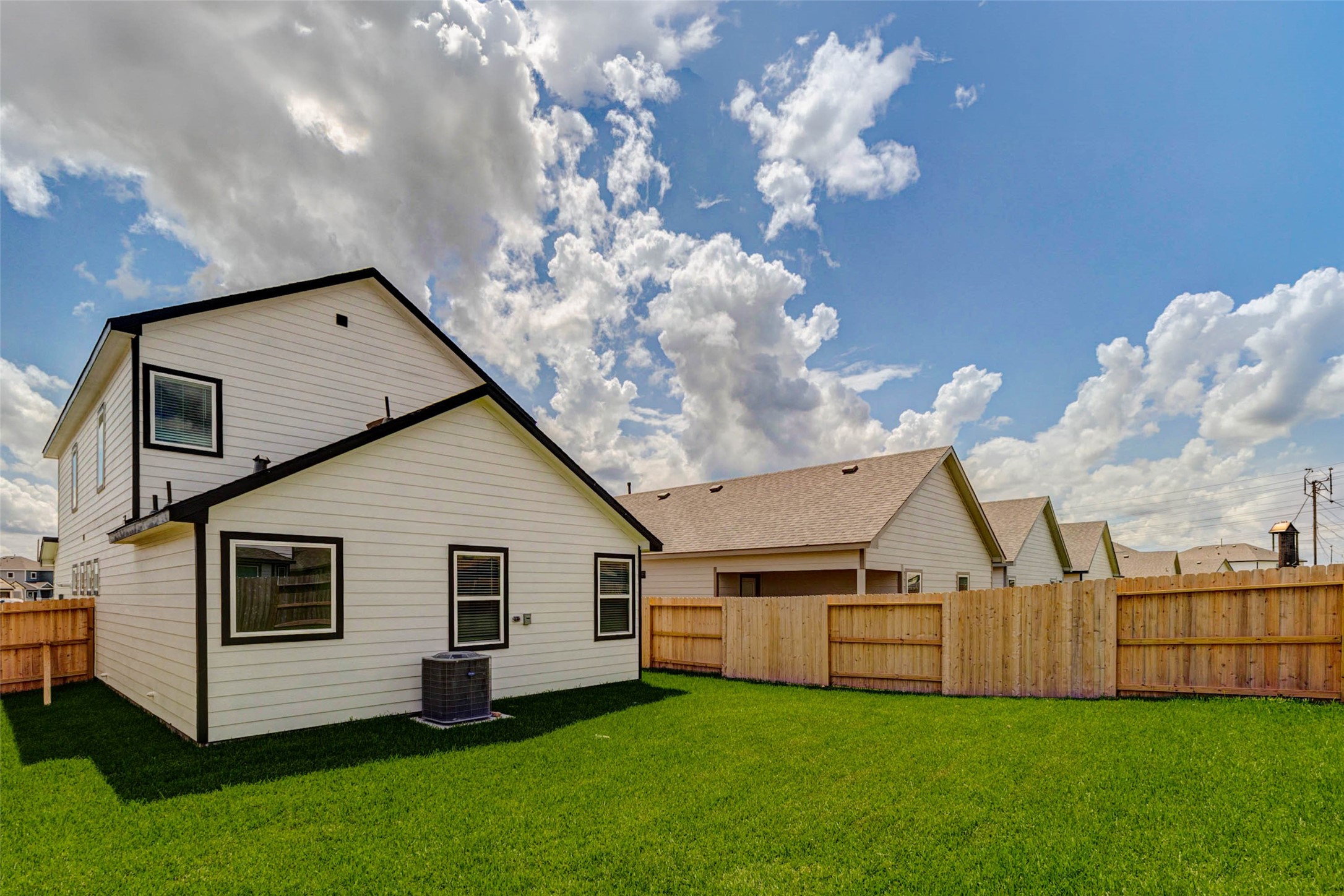 6471 Escondido Drive Rosharon, TX 77583 - Photo 32 of 33 Angled backyard view featuring a wide green lawn, full wood privacy fencing, rear home elevation, and open sky above. The outdoor area offers room for recreation, pets, gardening, or a future seating area, creating a practical extension of the home’s living space.