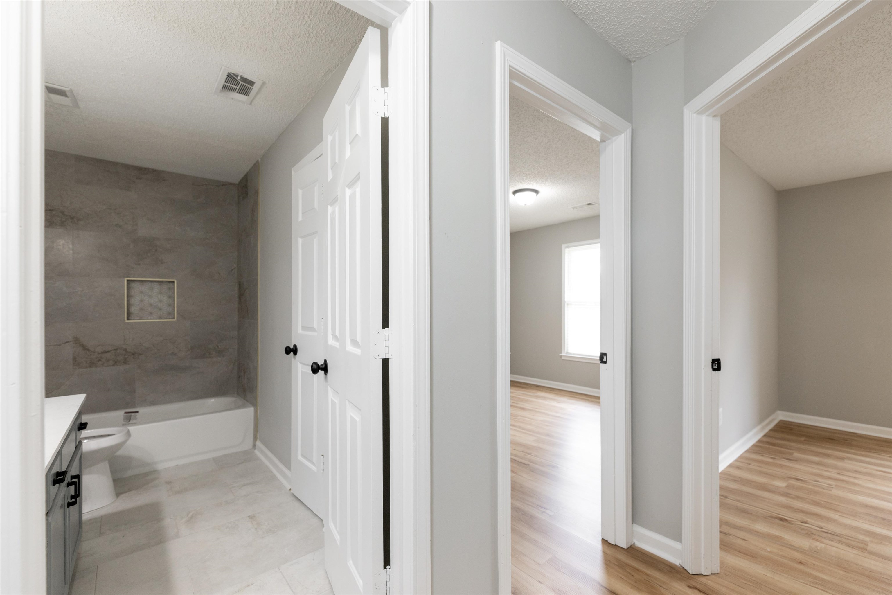7421 Richmond Road Memphis, TN 38125 - Photo 13 of 39 Hallway featuring a full bathroom with a tiled shower surround and a white bathtub, alongside two separate entrances to rooms with wood-finish flooring