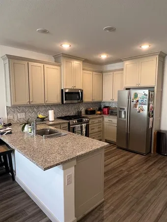 a kitchen with stainless steel appliances granite countertop a refrigerator a oven a sink dishwasher and white cabinets with wooden floor