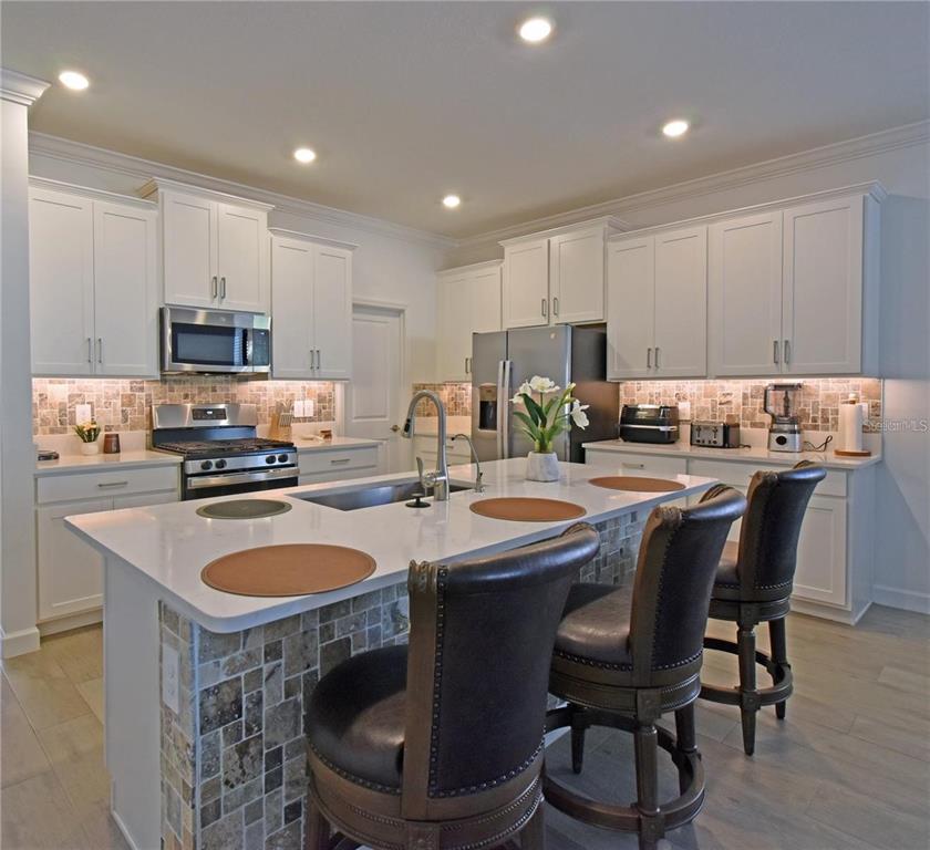 17304 Banded Gold Lane Wimauma, FL 33598 - Photo 13 of 44 a kitchen with kitchen island granite countertop a sink a stove a oven a dining table and chairs