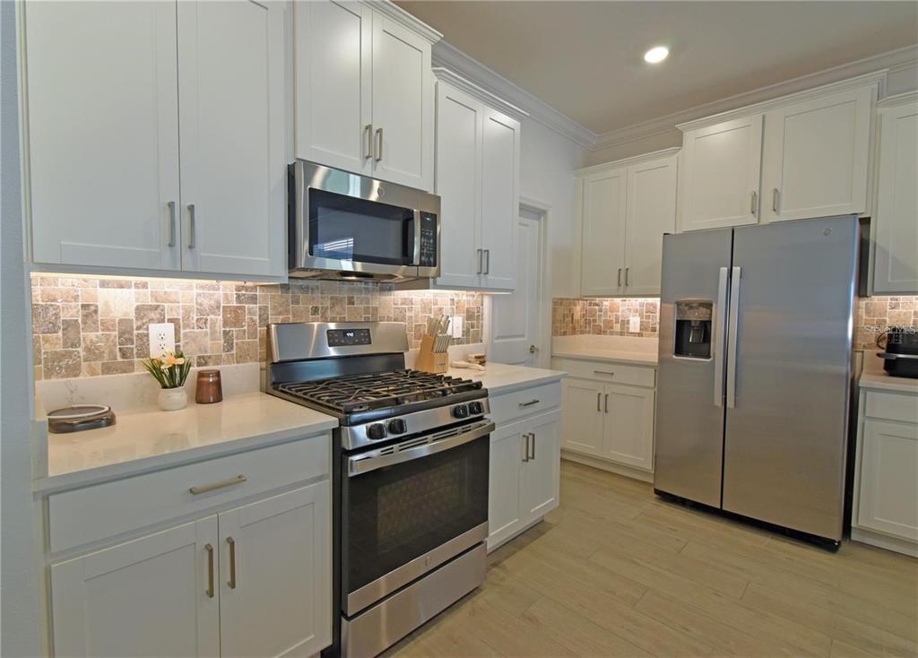 17304 Banded Gold Lane Wimauma, FL 33598 - Photo 17 of 44 a kitchen with stainless steel appliances white cabinets white stove a microwave and a refrigerator