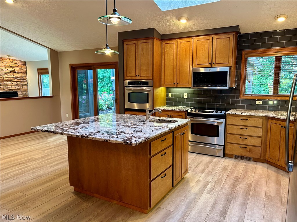 8763 Timber Edge Drive North Ridgeville, OH 44039 - Photo 5 of 40 Kitchen featuring light wood-type flooring, a center island with sink, appliances with stainless steel finishes, pendant lighting, and sink