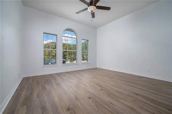 an empty room with wooden floor fan and windows