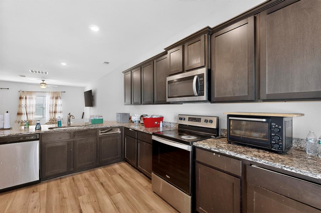 148 Point Rider Road Newark, TX 76071 - Photo 11 of 40 Kitchen featuring dark brown cabinets, appliances with stainless steel finishes, light stone countertops, light wood finished floors, and recessed lighting