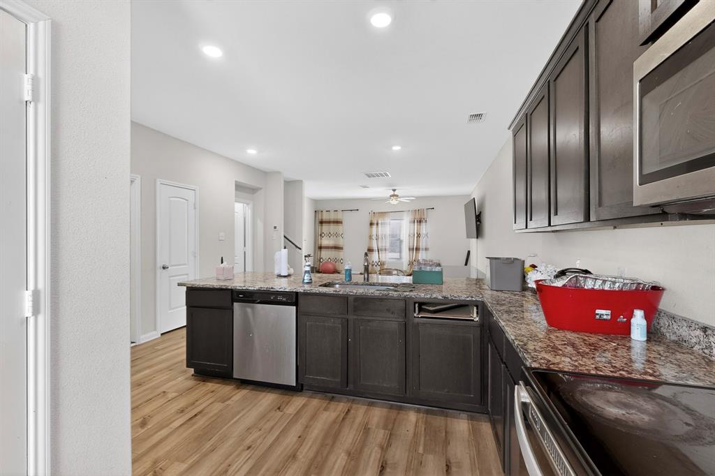 148 Point Rider Road Newark, TX 76071 - Photo 12 of 40 Kitchen with appliances with stainless steel finishes, dark stone counters, a peninsula, light wood finished floors, and dark brown cabinetry