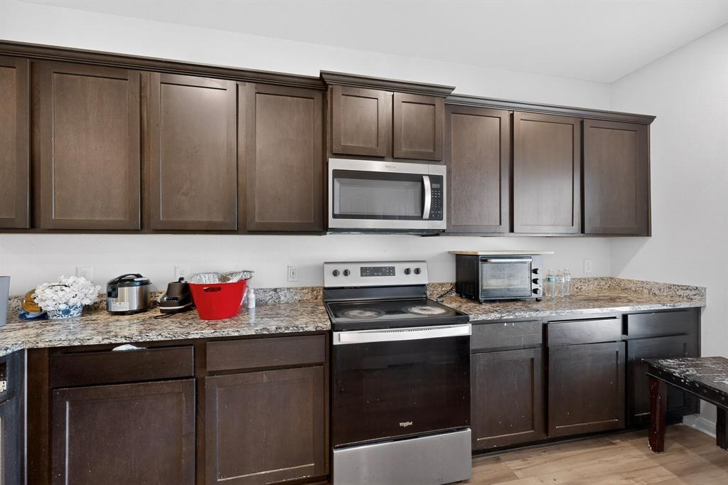 148 Point Rider Road Newark, TX 76071 - Photo 10 of 40 Kitchen featuring stainless steel appliances, dark brown cabinetry, light stone countertops, and light wood finished floors