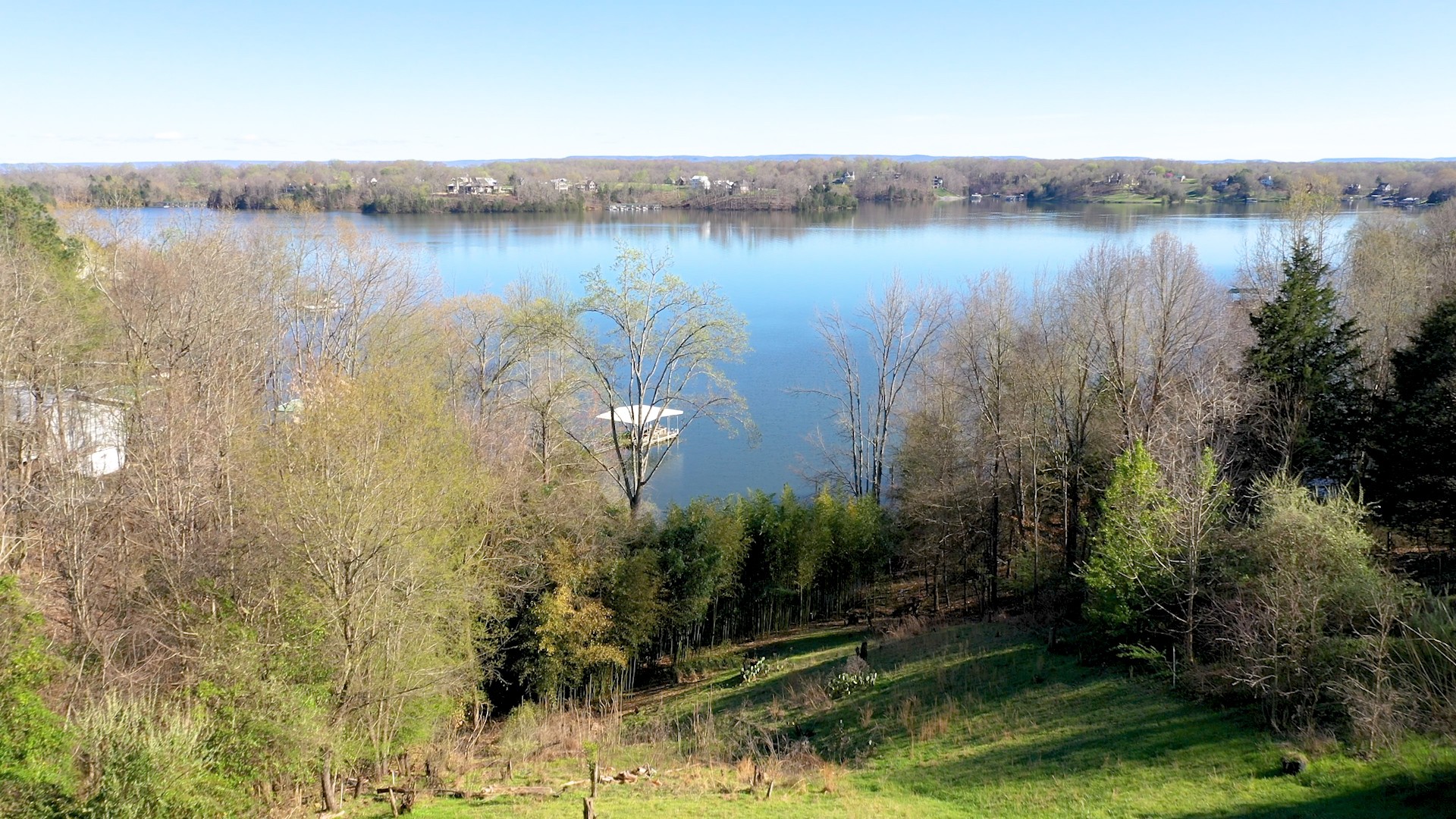 a view of a lake with a yard and trees in the background