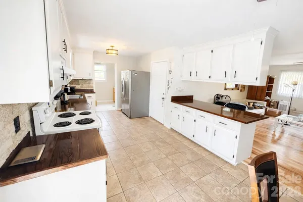 a kitchen with stainless steel appliances a stove a sink a refrigerator white cabinets and couches with wooden floor