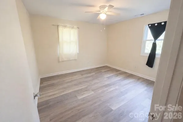 an empty room with wooden floor fan and windows