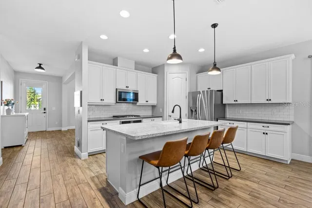 a open kitchen with stainless steel appliances granite countertop a stove a refrigerator a kitchen island a sink white cabinets and chairs