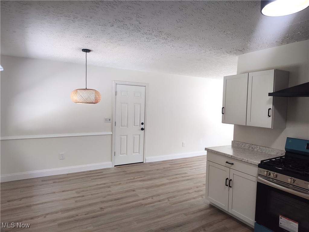 8016 Ninevah Road Geneva, OH 44041 - Photo 27 of 45 Kitchen featuring gas range, light countertops, light wood-type flooring, a textured ceiling, and white cabinetry
