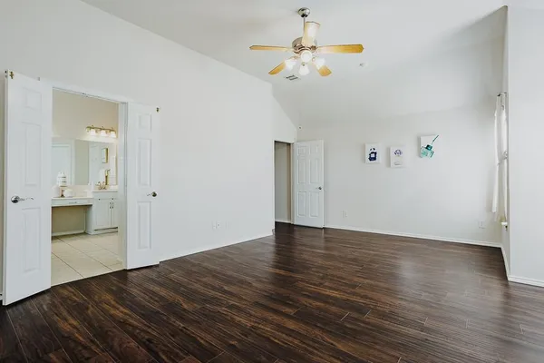 a view of an empty room with wooden floor and a kitchen