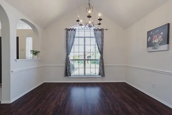 an empty room with wooden floor chandelier and windows