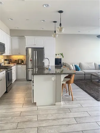 a kitchen with stainless steel appliances kitchen island granite countertop a stove a refrigerator and white cabinets with wooden floor