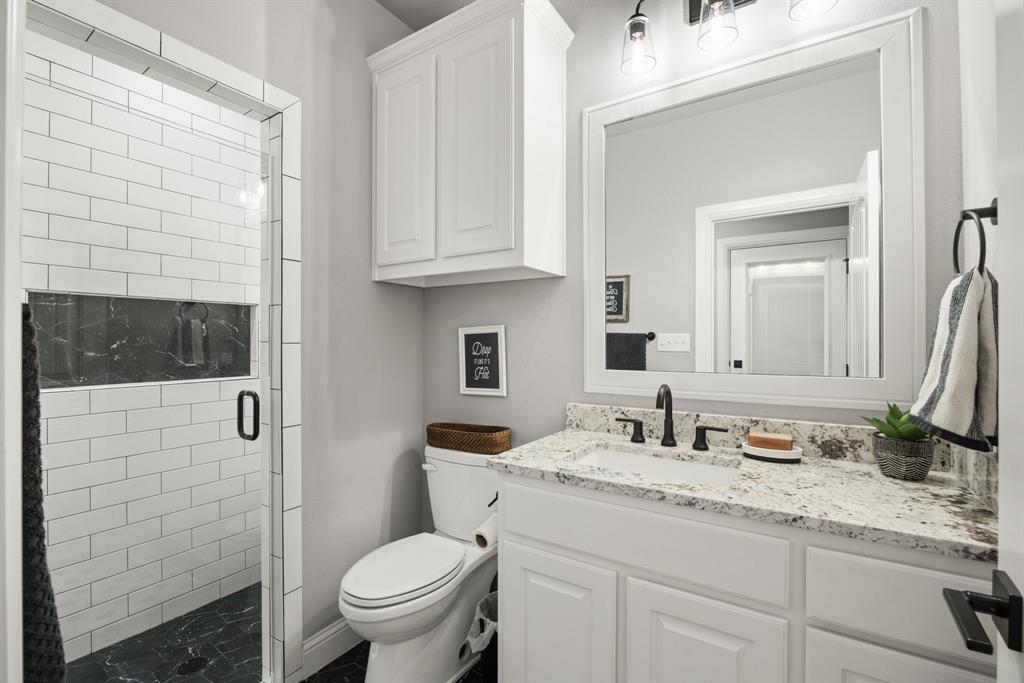 1800 Knox Road Tolar, TX 76476 - Photo 19 of 38 Bathroom #2 featuring a glass-enclosed shower with subway tile, built-in shower niche with dark stone accent, white vanity with stone countertop, under-mount sink, and matte black fixtures