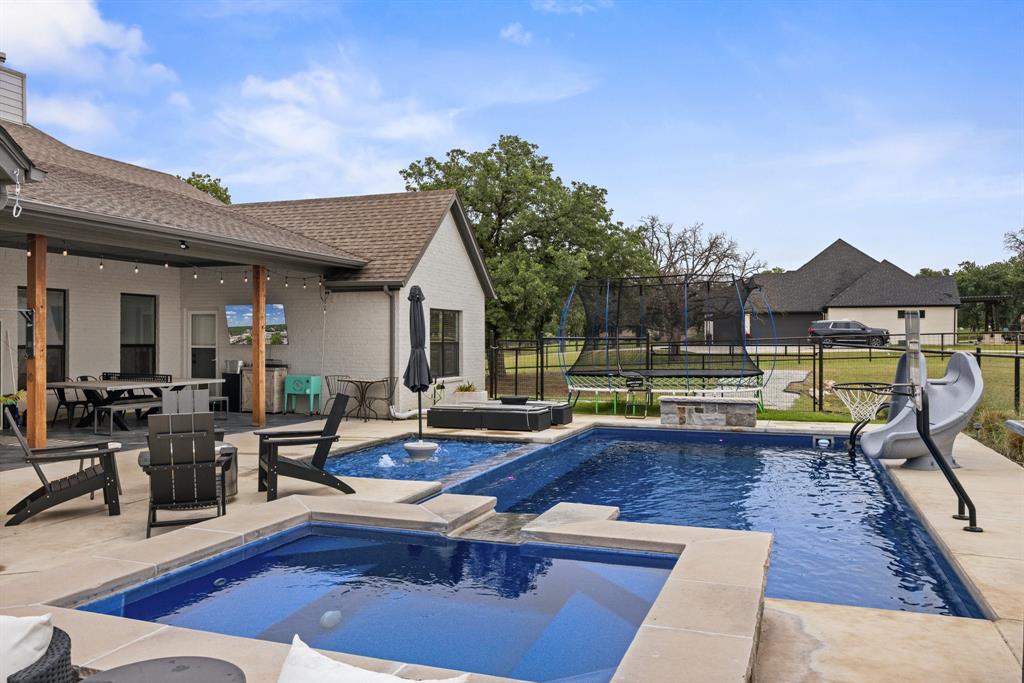 1800 Knox Road Tolar, TX 76476 - Photo 30 of 38 Expansive outdoor living area featuring a multi-level swimming pool, integrated spa, and a covered patio with string lighting
