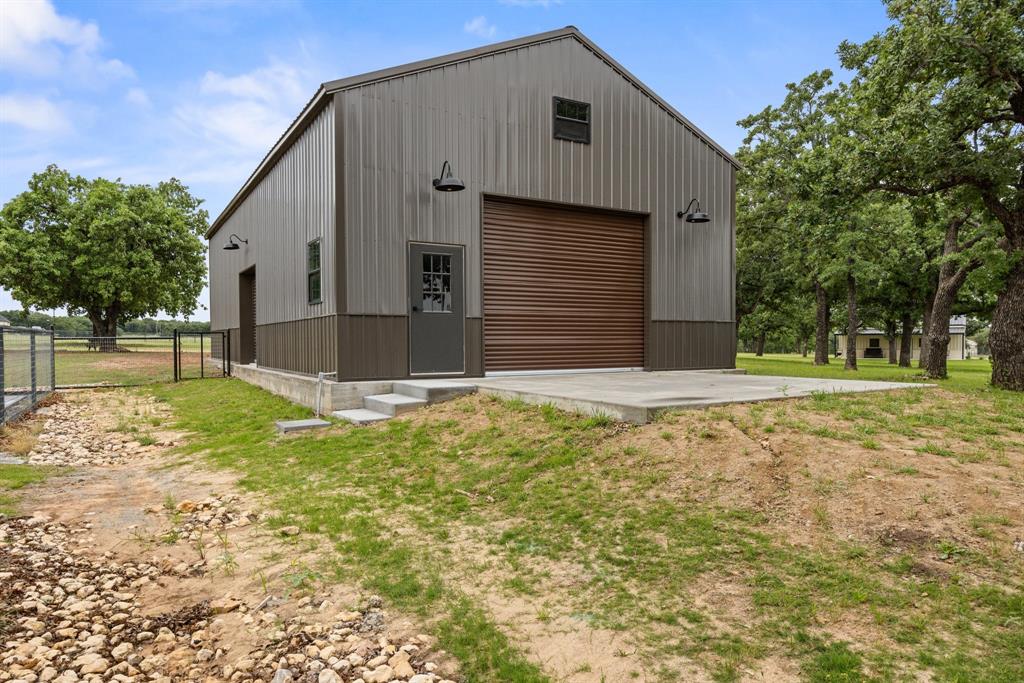 1800 Knox Road Tolar, TX 76476 - Photo 34 of 38 Metal-sided outbuilding featuring a two-tone facade, a large brown roll-up doors, one on each end along with small roll up door on side. Shop has an entryway door and shop has electricity.